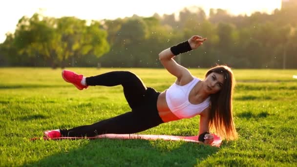 Nő, csinál hasi crunches edzés a fitness szőnyeg, nyáron a parkban, lassú mozgás, a naplemente. - Felvétel, videó