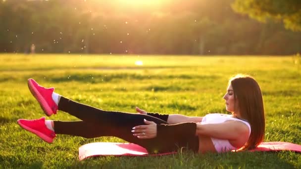 Kobieta robi ćwiczenia brzucha brzuszków na maty fitness lato w parku w zwolnionym tempie o zachodzie słońca. - Materiał filmowy, wideo