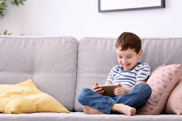Cute little boy with mobile phone on sofa at home - Photo, Image