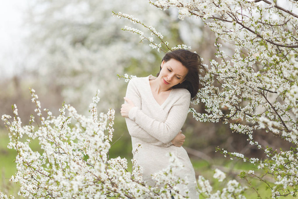 Молодая расслабленная нежная очаровательная женщина в легкой повседневной одежде, держась за руки, стоящие в городском саду или парке на цветущем дереве. Весна природа, цветы. стиль жизни, концепция досуга
 - Фото, изображение