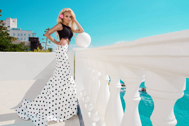 Mooie, sexy vrouw in een elegante polka-dot jurk, permanent bij het zwembad - Foto, afbeelding