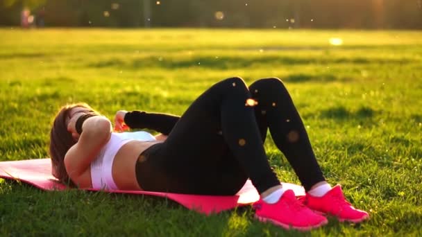 Mujer haciendo ejercicios abdominales en la colchoneta del parque de verano en cámara lenta al atardecer
. - Imágenes, Vídeo