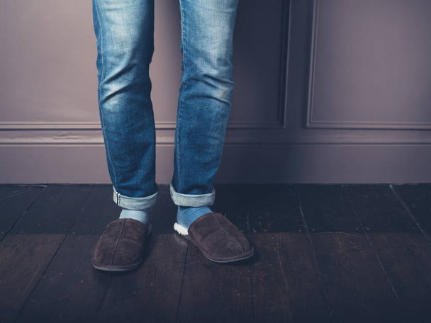 The legs and feet of a young man with warm slippers on a wooden floor - Photo, Image