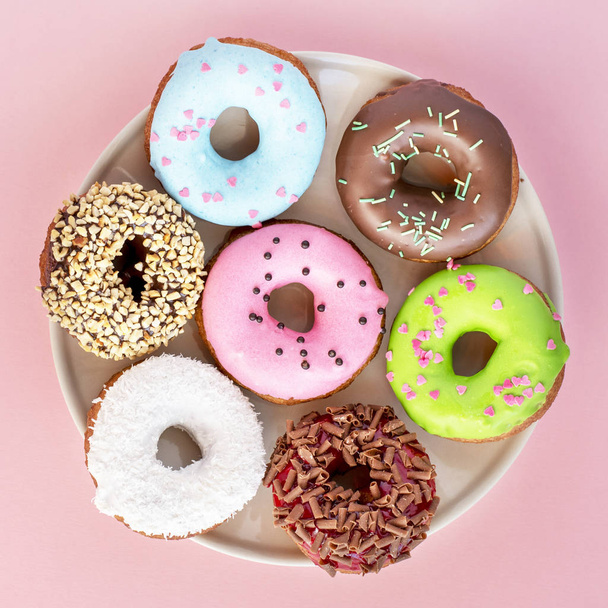 Set of donuts covered with a variety of glaze and sprinkled with sweets on a plate on a pink background - Zdjęcie, obraz