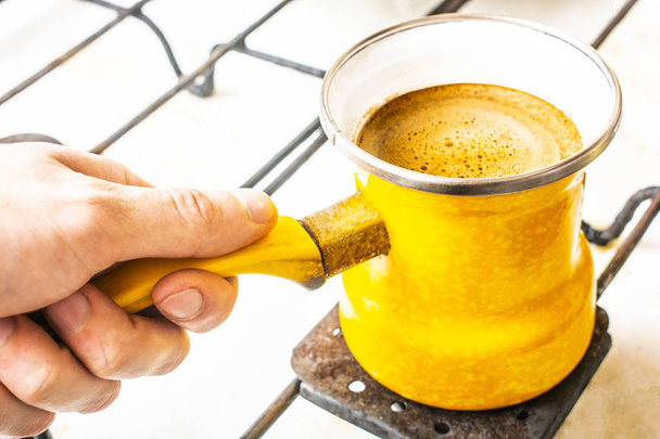 in his hand a yellow Turk with coffee on the stove. - Photo, Image
