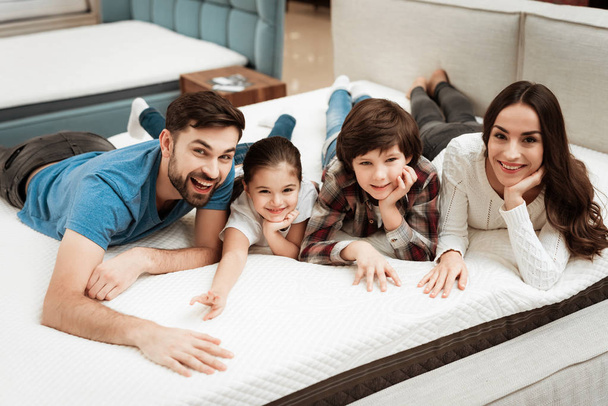 family checking softness of orthopedic mattress and lying on bed in furniture store - Photo, image