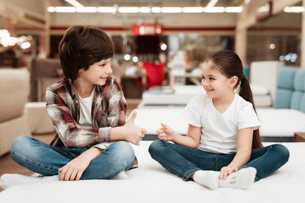 мальчик и улыбающаяся девушка показывают большие пальцы на ортопедическом матрасе в магазине
 - Фото, изображение
