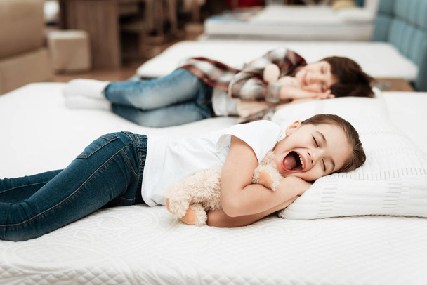 girl hugging bear and lying on bed with brother in mattress store - Photo, Image