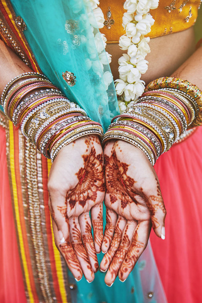 The close-up shot of Indian bride with beautiful saree in yellow blouse and red legenha showing hand with mehndi painted (henna) with a lot of glitter bracelets (bangle) on her wrist - Fotoğraf, Görsel