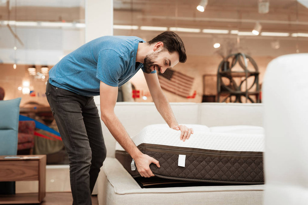 Young bearded man testing mattress in furniture store - Foto, Bild