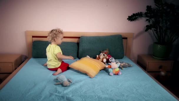 Csintalan gyerek dobás játékok ágyon a hálószobában. - Felvétel, videó