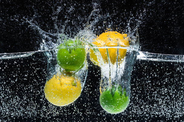 close up view of fresh lemons and limes in water isolated on black - Foto, Bild