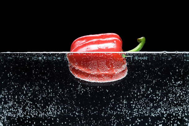 close up view of ripe red bell pepper in water isolated on black - 写真・画像