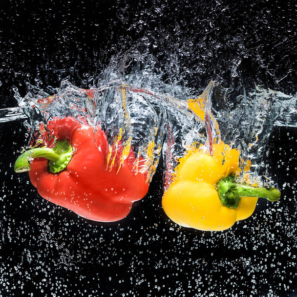 close up view of red and yellow bell peppers in water isolated on black - Fotografie, Obrázek
