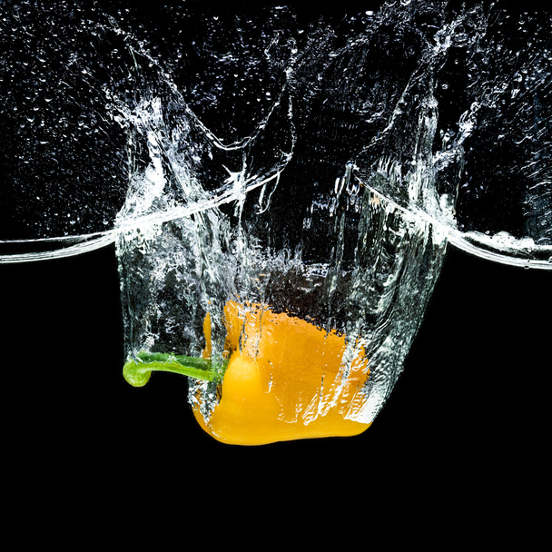 close up view of motion of yellow bell pepper falling into water isolated on black - Photo, Image
