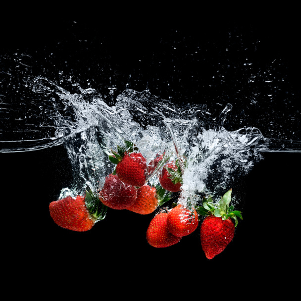 close up view of motion of ripe strawberries falling into water isolated on black - Fotografie, Obrázek