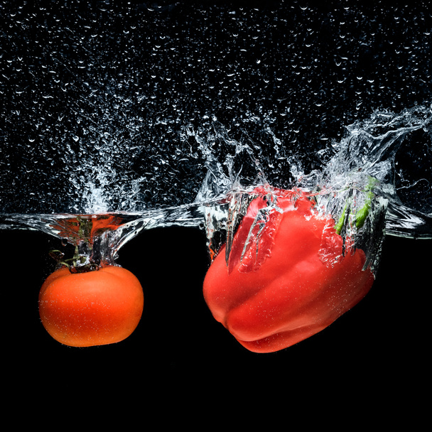vue rapprochée du poivron et de la tomate tombant dans l'eau isolée sur noir
 - Photo, image
