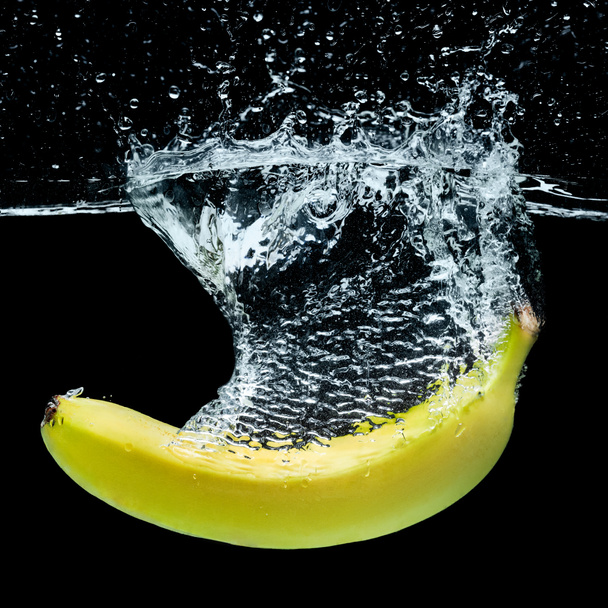 Nahaufnahme von Banane im Wasser mit Spritzern isoliert auf schwarz - Foto, Bild