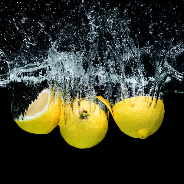 close up view of fresh lemons in water with splashes isolated on black - Foto, immagini