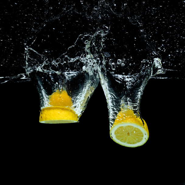 close up view of fresh lemon pieces in water with splashes isolated on black - Foto, immagini