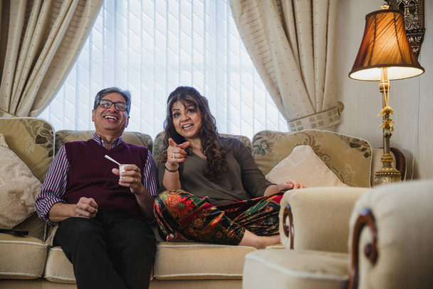 Mature couple are relaxing at home, watching television in the living room.  - Foto, afbeelding