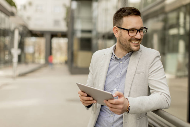 Handsome young businessman with digital tablet by the office building - Fotoğraf, Görsel