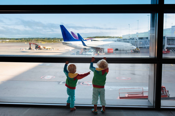 Παιδιά στο αεροδρόμιο. Τα παιδιά κοιτάνε το αεροπλάνο. Ταξιδεύει και πετάει με παιδί. Οικογένεια στην πύλη αναχώρησης. Διακοπές και ταξίδια με μικρό παιδί. Αγόρι και μωρό πριν την πτήση στο τερματικό. Τα παιδιά πετάνε αεροπλάνο.. - Φωτογραφία, εικόνα