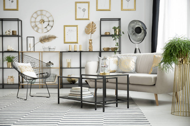 Pillows with gold pattern on beige sofa and metal armchair in bright living room interior with gold and black furniture - Φωτογραφία, εικόνα