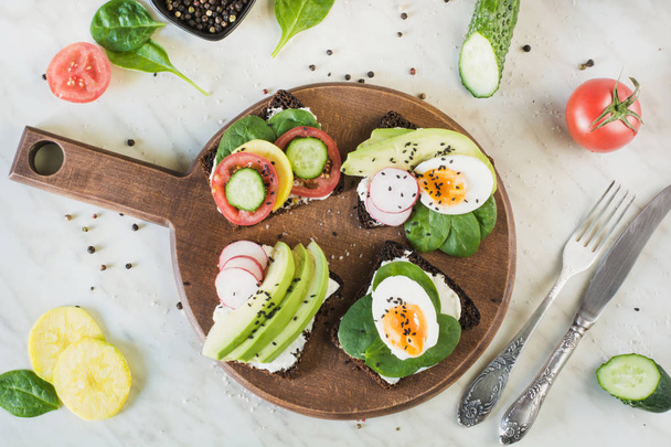 Summer sandwiches with fresh vegetables, eggs, avocado, tomato, rye bread on light marble table. Top vew. Appetizer for party. Flat lay. - Φωτογραφία, εικόνα