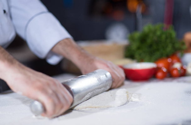 chef preparing dough for pizza rolling with rolling pin on sprinkled with flour table - Foto, imagen