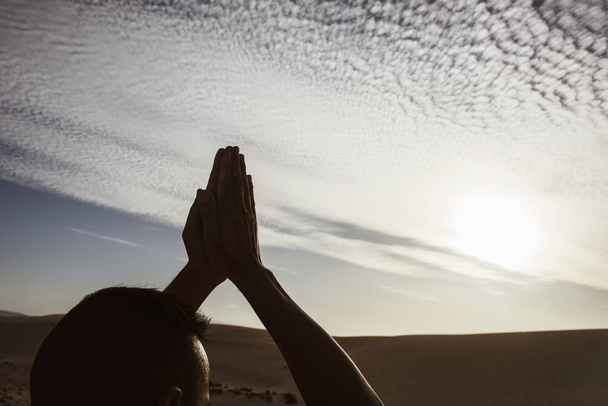 Close-up van een jonge blanke man beoefenen van yoga buiten, tegen een bewolkte hemel, met de zon op de achtergrond - Foto, afbeelding