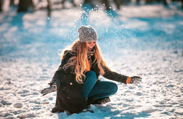 Smiling young woman throwing snow in the air at sunny winter day - Foto, Imagen