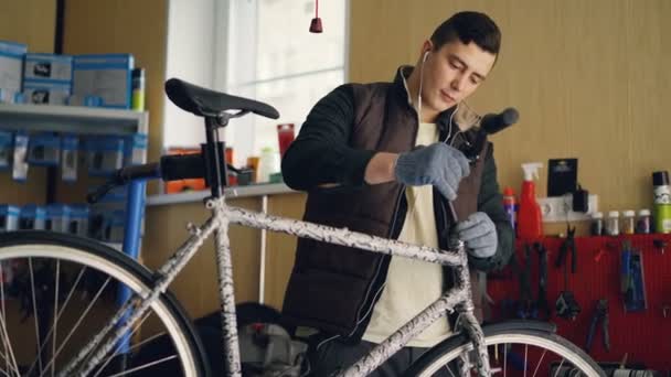 Focused mechanic is assembling bicycle placing handle-bar then tightening joints with key and listening to music through earphones. People and maintenance concept. - Кадри, відео