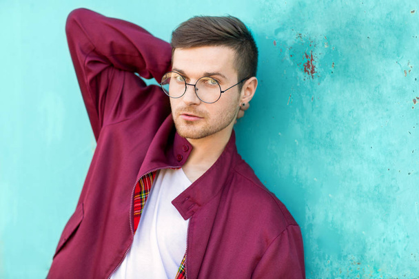 fashion hipster guy in glasses poses near the wall the color of the sour wave at sunset - Фото, изображение