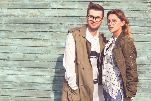 fashion couple in glasses with glasses in green clothes posing on blue wooden wall - Fotó, kép