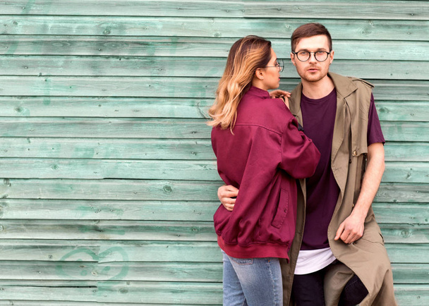 fashion couple in their glasses with burgundy clothes posing on a blue wooden wall - Фото, изображение