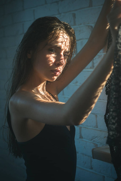 Beauty girl with natural look and healthy skin. Woman in black bodysuit at window. Woman with long wet or oily hair. Fashion model in fashionable lingerie. Beauty, fashion and look. - 写真・画像