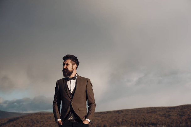 Fashion businessman wear classic coat with bow tie. Bearded man on cloudy sky. Hipster with beard and mustache on unshaven face. Freedom and success. Vacation, travelling and wanderlust, copy space. - Fotoğraf, Görsel