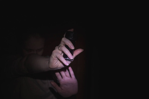 μια γυναίκα που κρατάει ένα σπρέι πιπεριού αερίου στο σκοτάδι, μαύρο λεμονάτα - Φωτογραφία, εικόνα