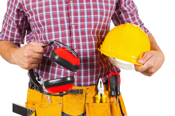 Close up picture of young carpenter with yellow tool belt holding safety helmet and headphones - Foto, Imagem