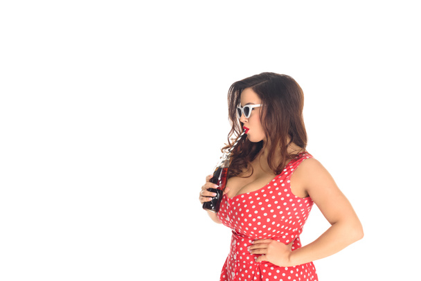 side view of stylish plus size woman in vintage sunglasses drinking soda isolated on white - Photo, image