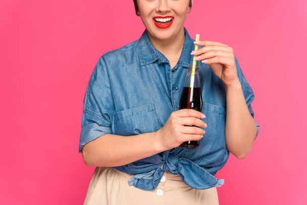 abgeschnittene Aufnahme einer lächelnden Pin-up-Frau mit Glasflasche und Trinkhalm isoliert auf rosa - Foto, Bild