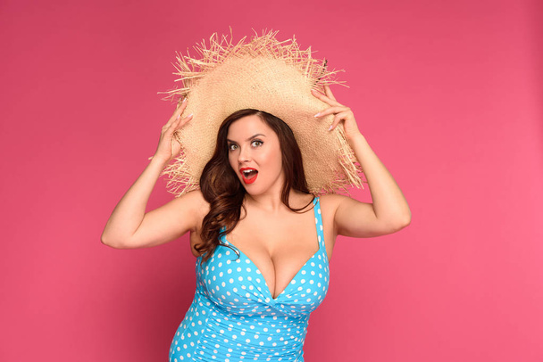 beautiful surprised size plus woman in straw hat looking at camera isolated on pink - Photo, Image