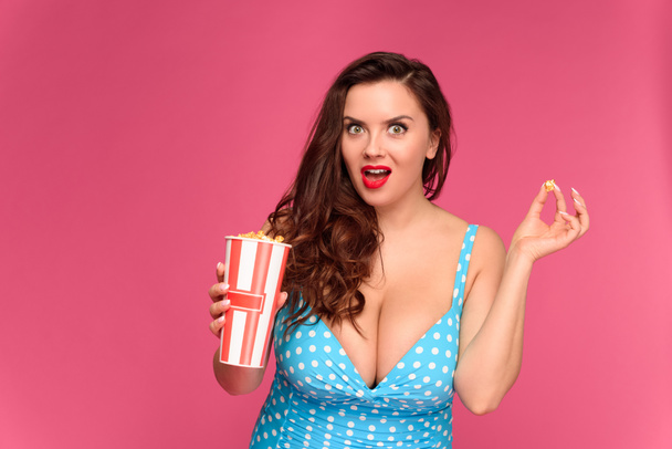 surprised young woman in swimsuit holding box of popcorn and looking at camera - Photo, Image