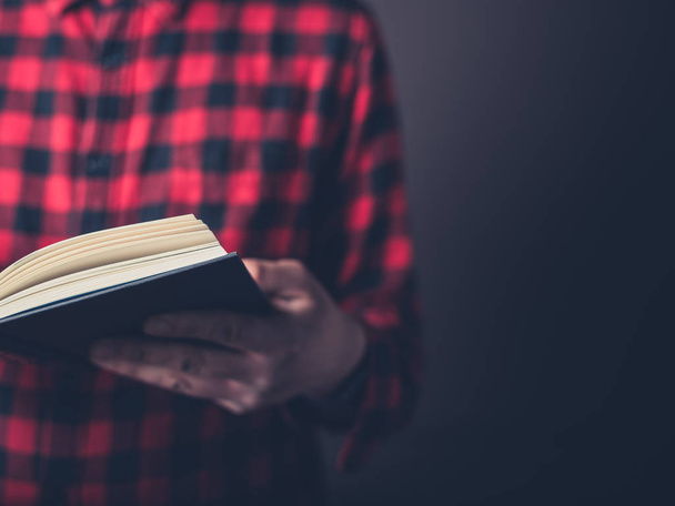 A young man wearing a flannel shirt is reading a book - Photo, image