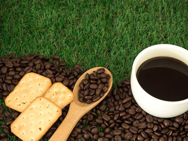 Чашка кави та кавових зерен на дерев'яній ложці та печиві на зеленому фоні трави
 - Фото, зображення