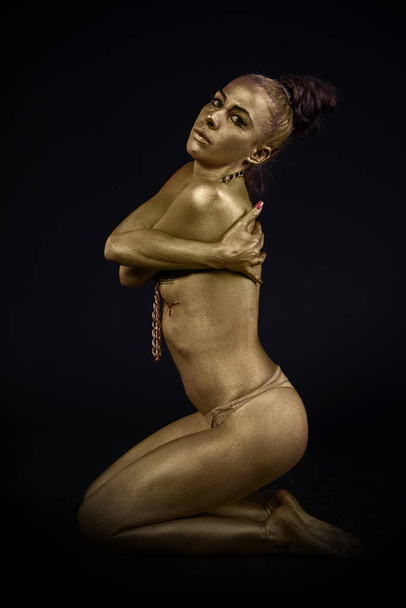 woman fully dressed in gold and font type in artistic position and  on black background - Fotoğraf, Görsel
