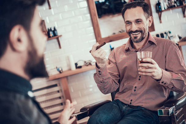 Client relaxing after haircut with beverage and cigar in barbershop - 写真・画像