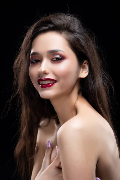 Portrait of a beautiful glamorous brunette girl sensually covers her naked breast with her hands. Shimmering makeup, red lips. Healthy smooth skin. Isolated on black. Copy space. - Foto, Imagem
