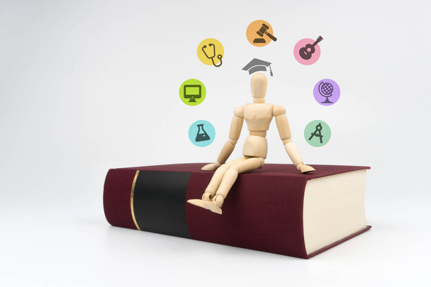 concetto di istruzione e laurea: figura di legno è seduto su un libro rosso con le icone di occupazione e cappello accademico quadrato intorno ad esso
 - Foto, immagini